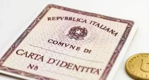 Primo piano di una carta d'identità cartacea italiana accanto a una moneta su sfondo bianco