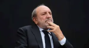 Uomo anziano in abito scuro con espressione pensierosa su sfondo nero