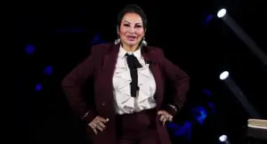 Una donna in abito elegante posa su un set televisivo con sfondo scuro e luci