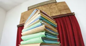 Una pila di fascicoli cartacei all'interno di un ufficio giudiziario con tende rosse
