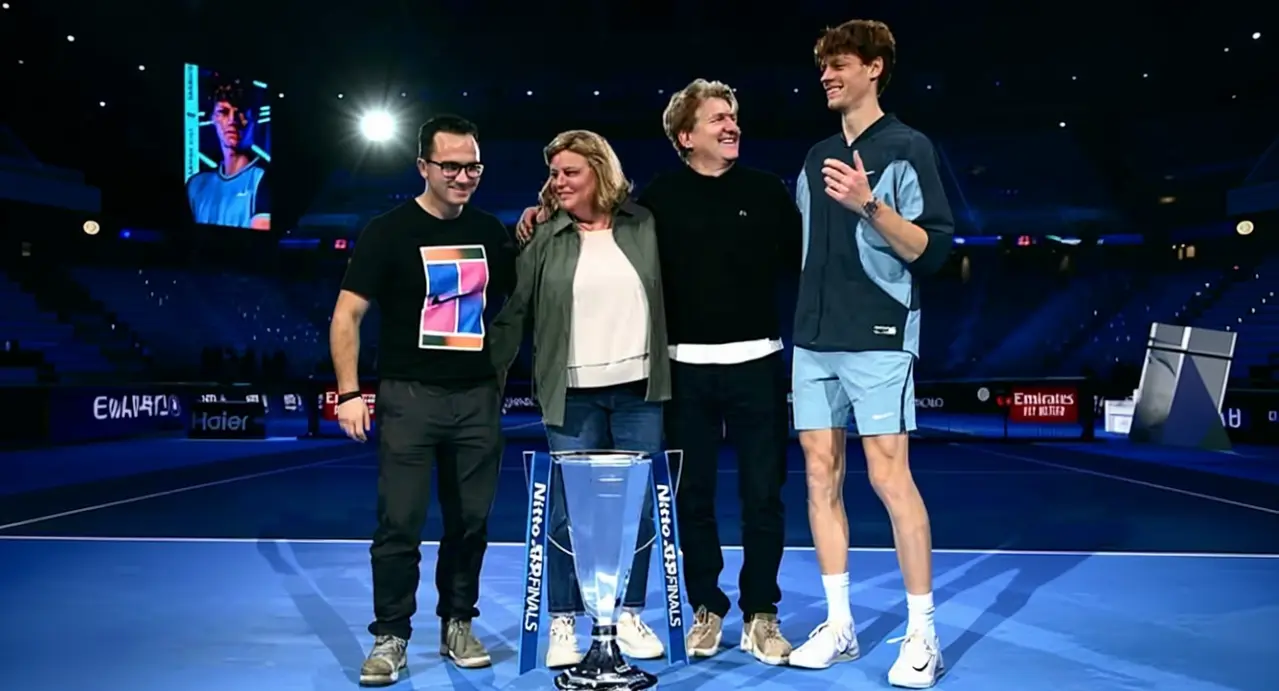 Una persona in abbigliamento sportivo sul campo da tennis con tre altre persone accanto a un trofeo
