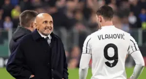 Un uomo in giacca scura parla con un calciatore in maglia bianca con il numero 9