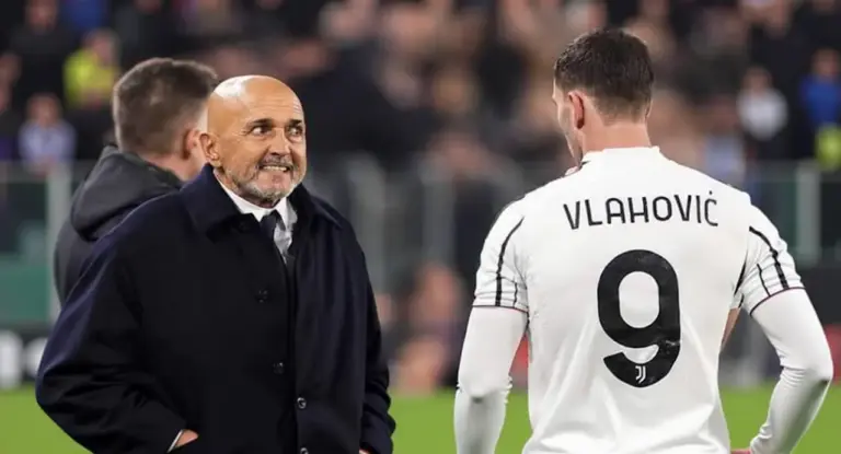 Un uomo in giacca scura parla con un calciatore in maglia bianca con il numero 9