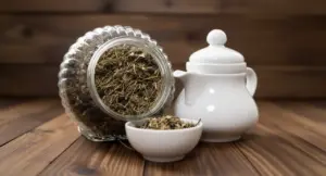 Barattolo di tisana secca con teiera bianca e ciotola su tavolo in legno